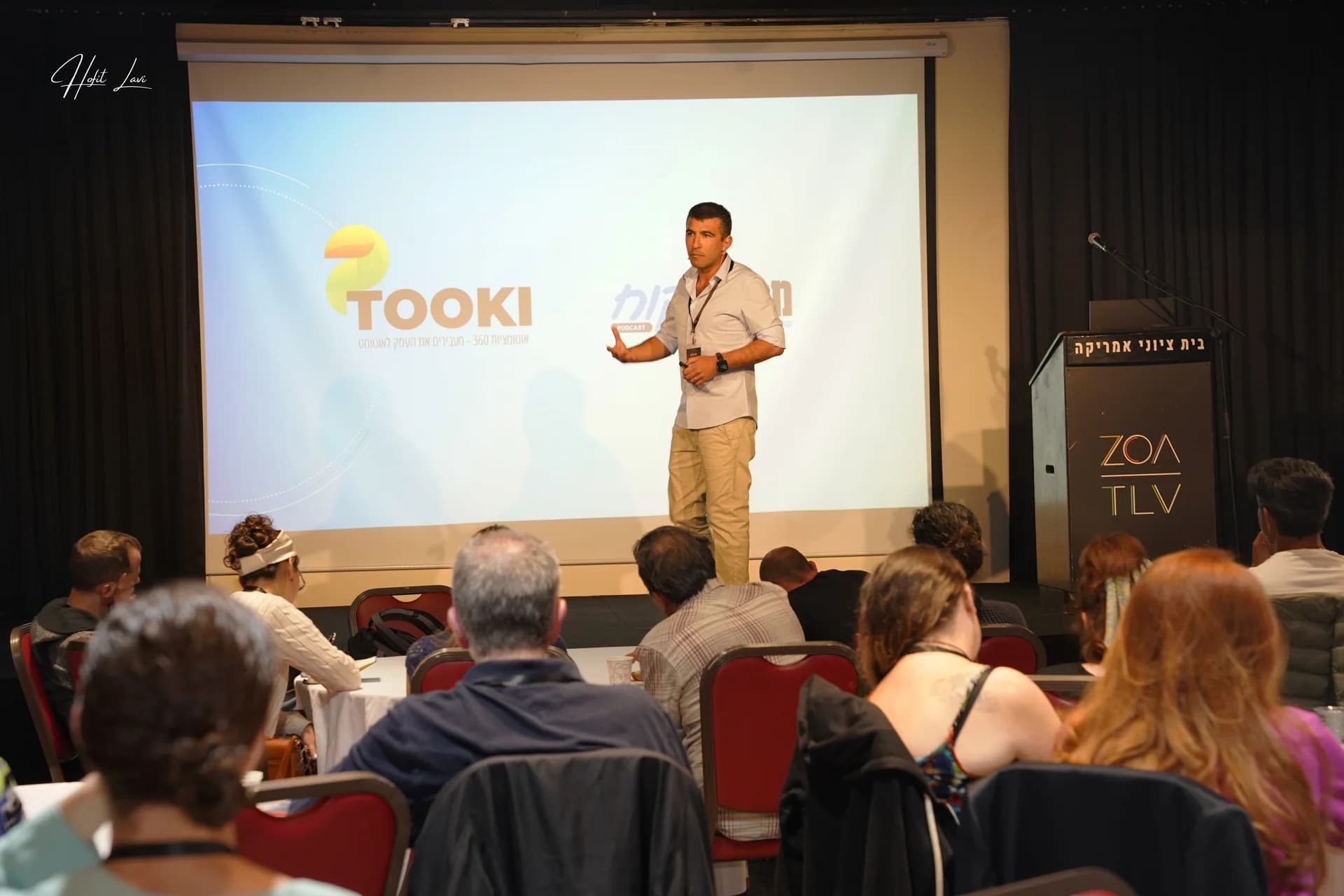 Dani presenting on stage in a white shirt, with an audience in the foreground