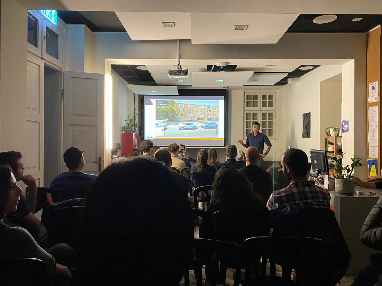 Dani presenting beside a projection screen in a classroom-style venue